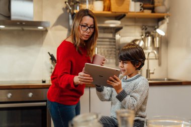 Anne ve oğlu mutfaktaki dijital tablette yemek tarifi arıyorlar.