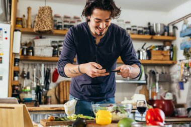 Adam blogcu mutfağında salata fotoğrafı çekiyor.