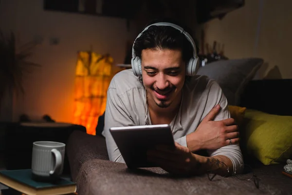Kulaklıklı Bir Adam Odasındaki Kanepede Yatarken Dijital Tablet Kullanıyor Merhaba — Stok fotoğraf