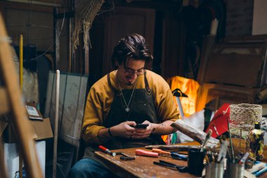 Adam atölyesinde otururken akıllı telefon kullanıyor.