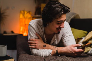 Annem evdeki kanepede uzanıyor ve cep telefonu kullanıyor.