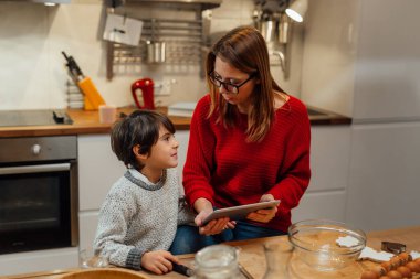 Anne ve çocuk mutfaktaki dijital tablette yemek tarifi arıyorlar.