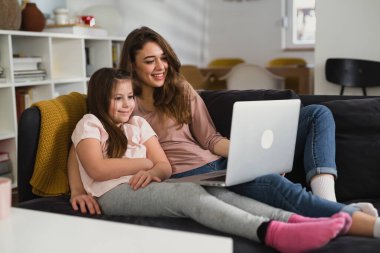 Anne ve kızı kanepede yatıyorlar ve dizüstü bilgisayar kullanıyorlar.