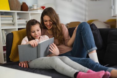 Anne ve kızı kanepede uzanıp kitap okuyorlar.