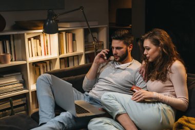 Çift kanepede oturuyor ve evde dizüstü bilgisayar kullanıyor.