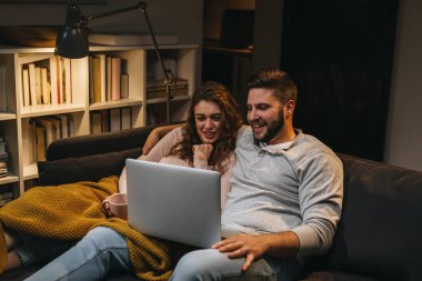 Çift kanepede oturuyor ve evde dizüstü bilgisayar kullanıyor.