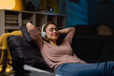 Kadın evde oturup kulaklıkla müzik dinliyor.