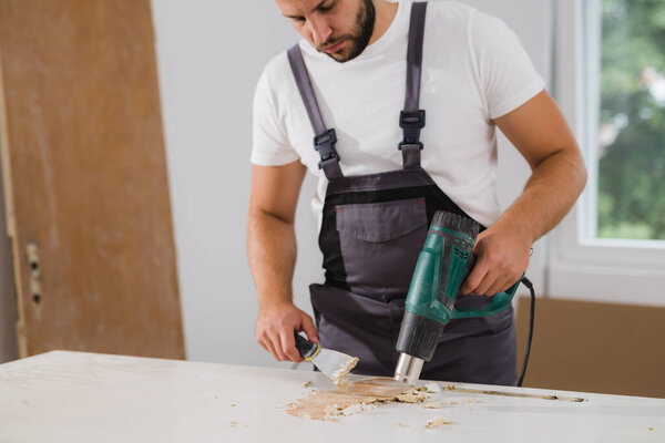 man using heat gun for removing old paint from door