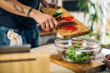 Adam mutfakta kırmızı biber kesiyor. Yemek için salata hazırlıyorum.