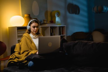 Oturma odasındaki koltukta otururken dizüstü bilgisayar kullanan bir kadın. Akşam atmosferi