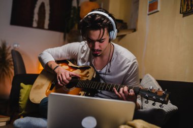 Adam odasında akustik gitar çalıyor. Çevrimiçi dersi var.