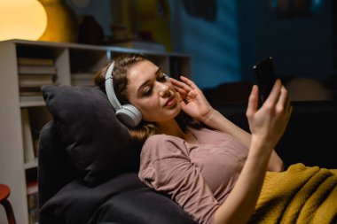 Oturma odasındaki koltukta otururken dizüstü bilgisayar kullanan bir kadın. Akşam atmosferi