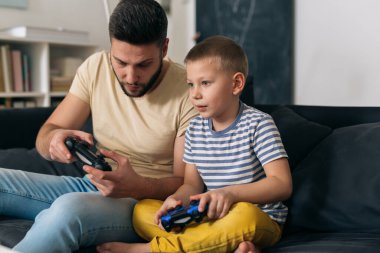 Baba ve oğul evdeki konsolda video oyunu oynuyorlar.