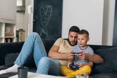 Baba ve oğul evdeki konsolda video oyunu oynuyorlar.