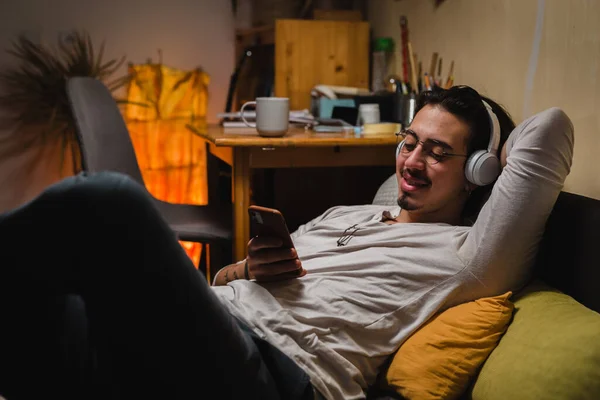 Чоловік Розслабляється Дивані Вдома Грає Своїм Телефоном Носить Навушники — стокове фото