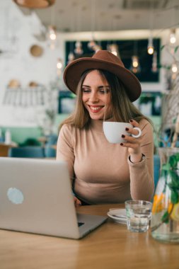 Kahve içen ve kafede dizüstü bilgisayar kullanan bir kadın.