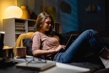 Evde dijital tablet kullanan bir kadın. Evdeki kanepede dinleniyorum.