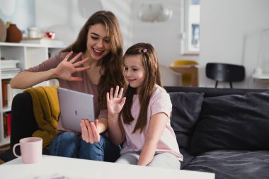 Anne ve kızı dijital tablet kullanarak evden sohbet ediyorlar.