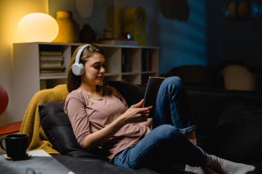Genç kadın dijital tablet kullanarak evde dinleniyor