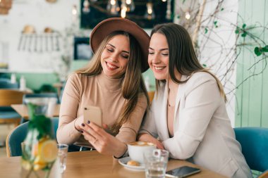 Kadın arkadaşlar kafeteryada cep telefonu kullanarak kahve molası veriyorlar.
