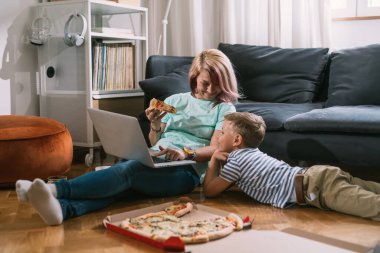Bekar anne ve oğul evde birlikte vakit geçiriyorlar, dizüstü bilgisayar kullanıyorlar ve pizza yiyorlar.