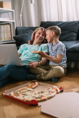 Küçük beyaz çocuk haftasonu annesiyle harika vakit geçiriyor. Dizüstü bilgisayarda film izlemek ve pizza yemek.