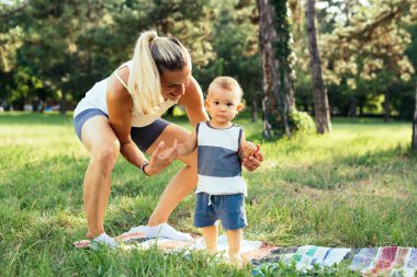 Genç beyaz bebek yürümeyi öğreniyor. Annesi yanında, onu tutuyor ve yardım ediyor.