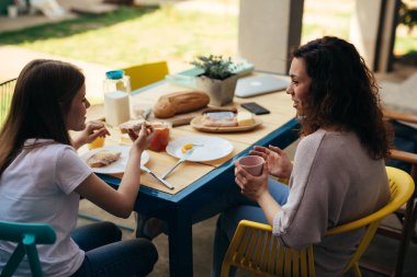 young girl talks with her mom while breakfast together outdoor