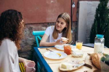 shoot of young woman holding sandwich while breakfast with her mother