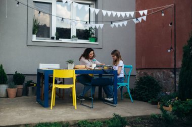 wide angel shoot of young caucasian mother and her daughter having breakfast outdoor in back yard