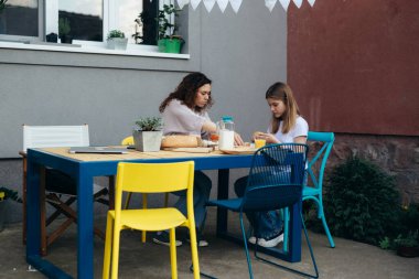 young caucasian mother and her daughter having breakfast outdoor in back yard