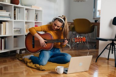 Genç bir kadın evde gitar çalmayı öğreniyor.