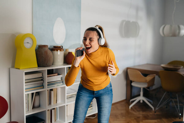 caucasian woman listening music on headphones and singing at home