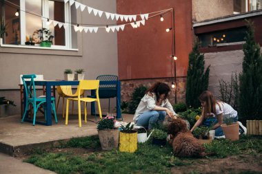 caucasian mother and her daughter gardening in their home backyard with companionship of their dog
