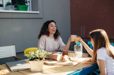 mother and her teenager daughter sitting table and having breakfast in backyard . they cheers with coffee and orange juice