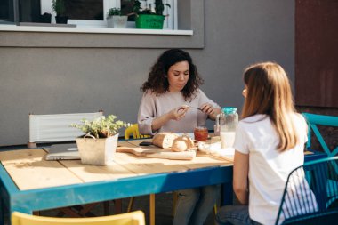 mother and her teenager daughter sitting table and having breakfast in backyard