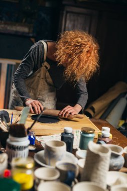Kafkasyalı kızıl saçlı kadın atölyesinde kil kaplar yapıyor.