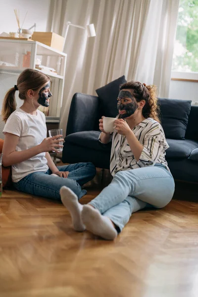 caucasian mother and daughter with cosmetic masks applied relaxing at home and talking