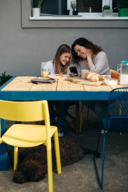caucasian mother and daughter enjoying time together during breakfast at home. they are using smart phone