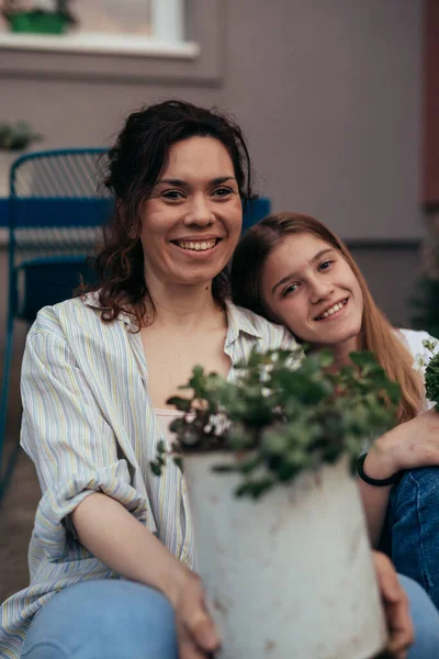 latin mother with her caucasian daughter smiling and looking at camera while gardening in home backyard