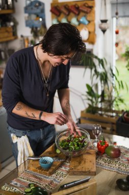 Evinin mutfağında salata çeşnili dövmeli adam.