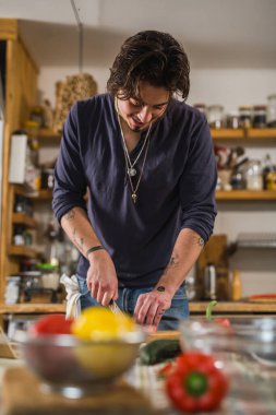 Genç, beyaz bir adam mutfağında sebze doğruyor.