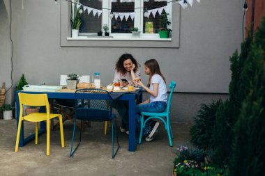 mother and daughter having breakfast on terrace in backyard
