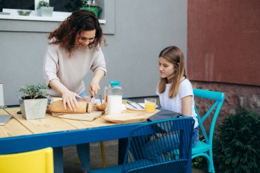mother and daughter breakfast together at home in backyard. mother cuts bread
