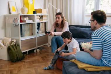 Genç, beyaz bir aile, oğluyla video oyunu oynayarak evde vakit geçiriyor.