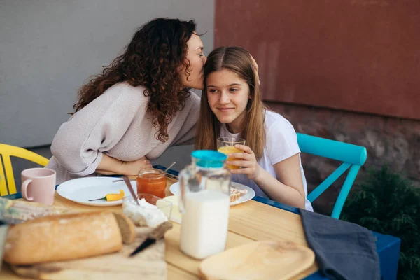 caucasian mother kisses her daughter while having breakfast outdoor in backyard