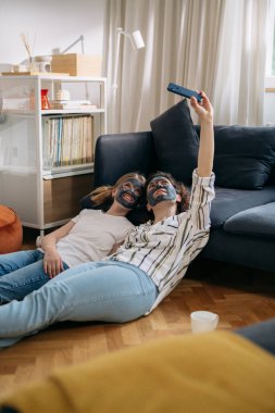 mother and daughter with applied cosmetic face mask having great time at home