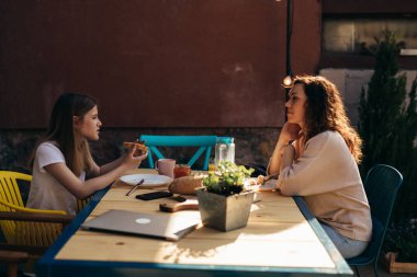 mother and daughter eating breakfast and talking in their home backyard