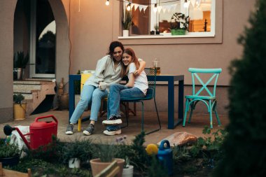Anne ve kızı masada oturup evlerinin arka bahçesinden konuşuyorlar. Sarılmıyorlar.