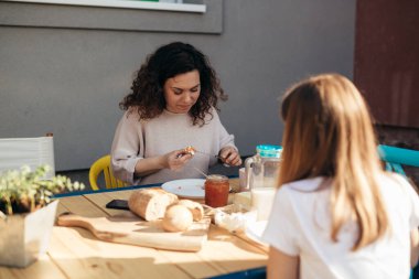 Anne ve kızı evlerinin arka bahçesinde kahvaltı ediyorlar.